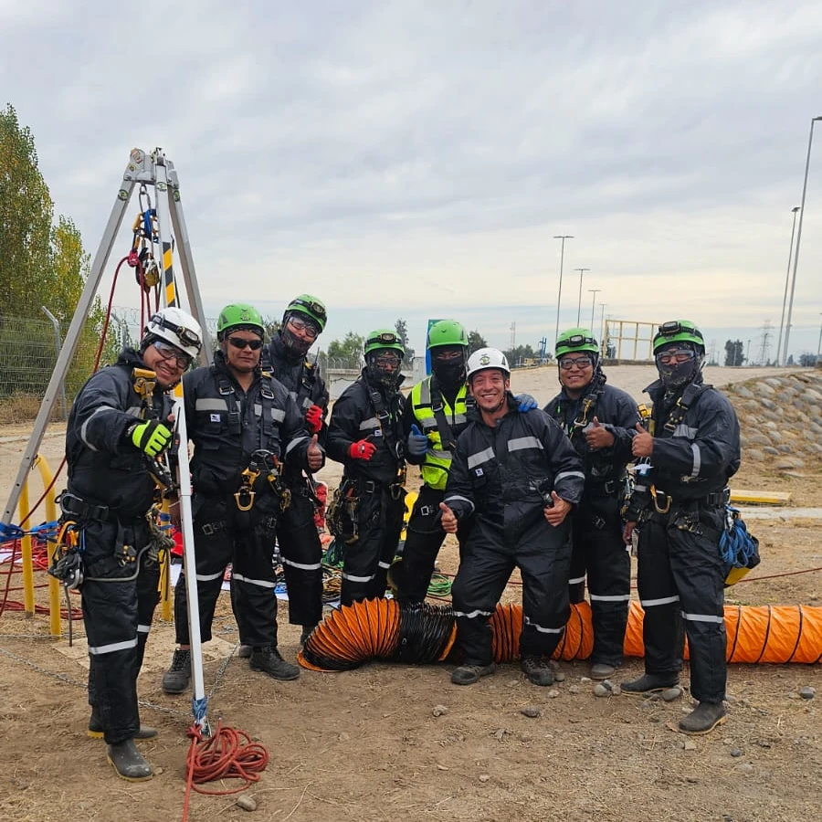 Un grupo de ocho trabajadores industriales al aire libre de Grupo Industrial, vistiendo trajes de seguridad negros con detalles reflectantes y cascos.